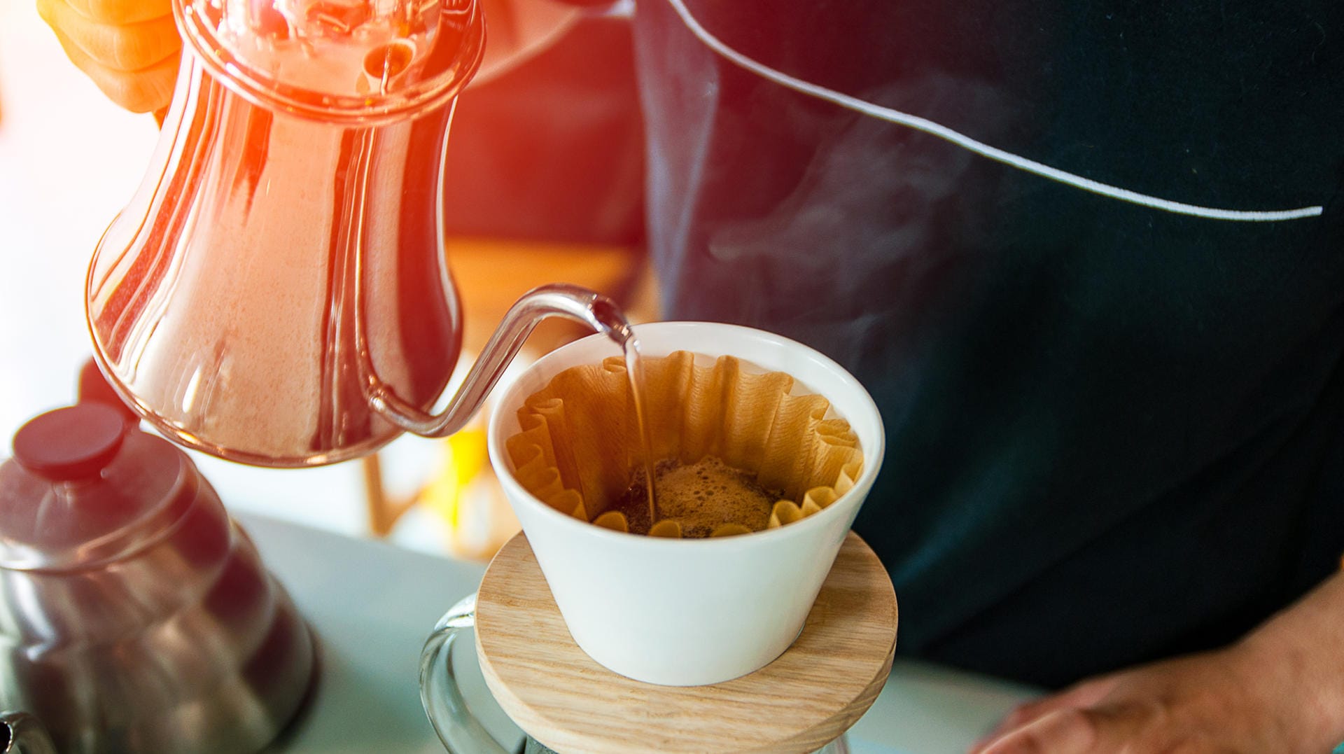 Ein Mann gießt Kaffee auf: Nach dem Quellen wird der Slow Coffee mit heißem Wasser aufgebrüht.