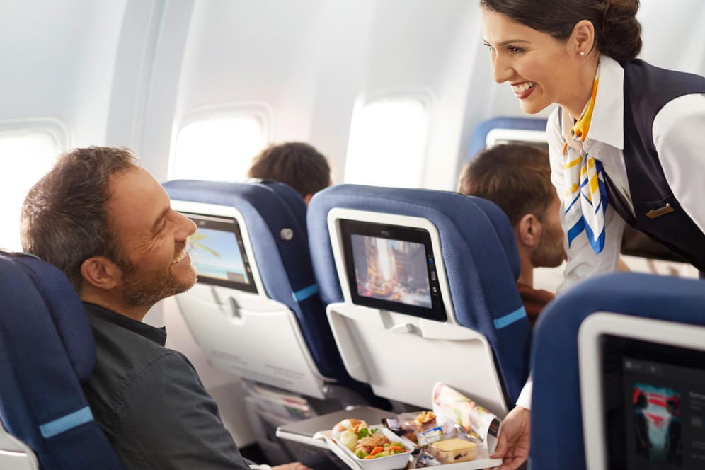 Fluggast und Stewardess in der Premium Economy Class: Viele Reisende empfinden das größere Platzangebot als Vorteil.