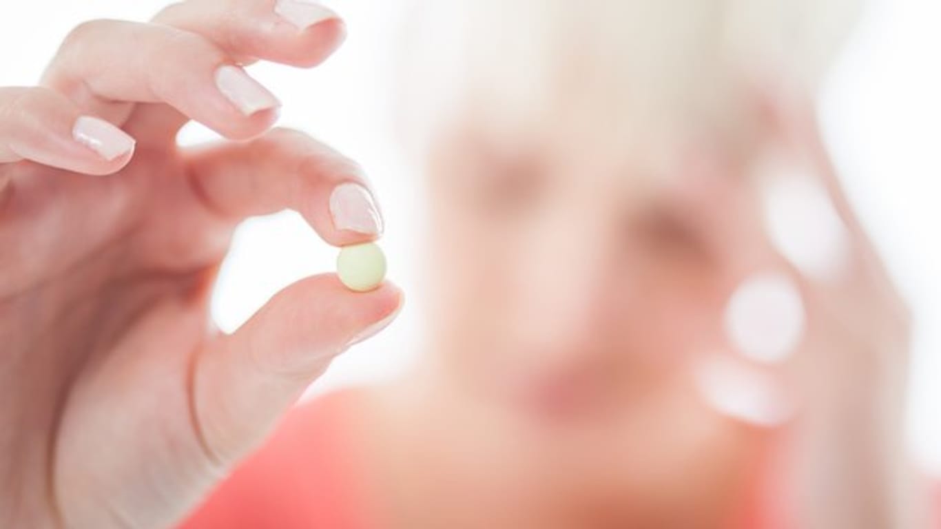Frau hält eine Tablette: Längstens drei Tage hintereinander und höchstens zehn Tage im Monat sollte man rezeptfrei erhältliche Schmerzmittel ohne ärztlichen Rat einnehmen.