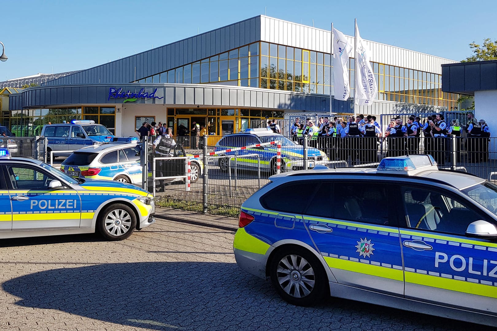 Zahlreiche Polizeifahrzeuge stehen vor dem Rheinbad: Nach der dreimaligen Räumung des Schwimmbads im Sommer enthüllt ein neuer Bericht der Stadtverwaltung Details zu den ersten beiden Tumulten.