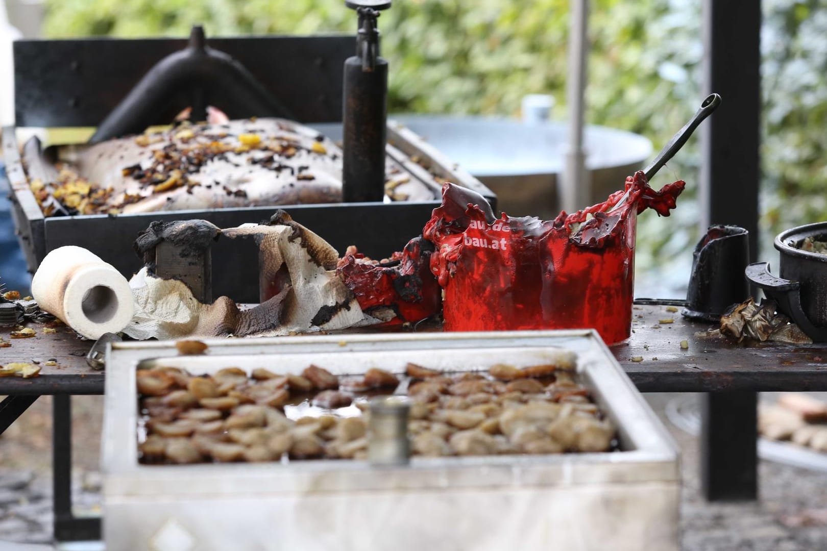 Verbrannte Grill-Utensilien sind auf einem Tisch auf dem Gelände eines Brauchtumsfestes im Siegerland zu sehen: Die Explosion einer übergroßen Bratpfanne hat ein zweites Todesopfer gefordert.