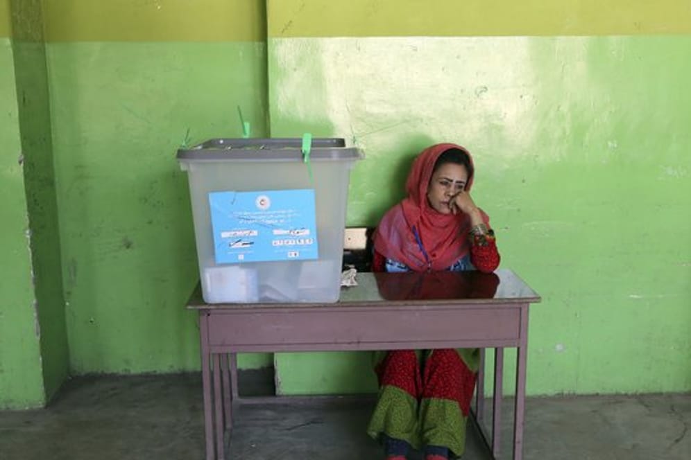 Eine Wahlhelferin sitzt in einem Wahllokal in Kabul neben einer Wahlurne.