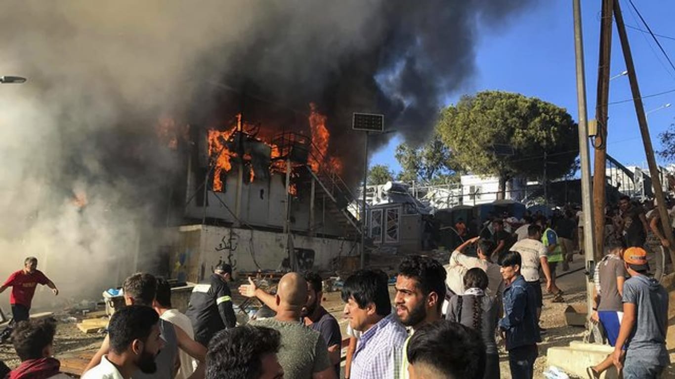 Migranten und Flüchtlinge stehen neben brennenden Hauscontainern.