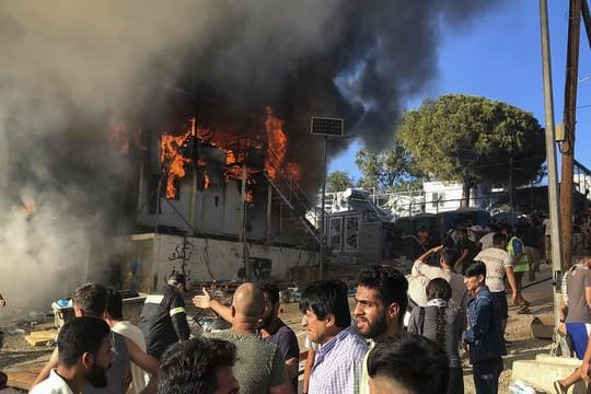 Migranten und Flüchtlinge stehen neben brennenden Hauscontainern.
