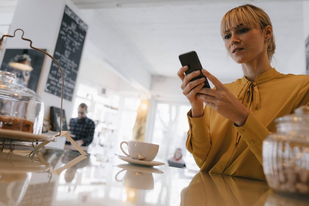 Eine junge Frau schaut im Café auf ihr Smartphone: Die Bundesnetzagentur hat Vodafone verboten, zu hohe Gebühren für die Telefonnummermitnahme zu kassieren.