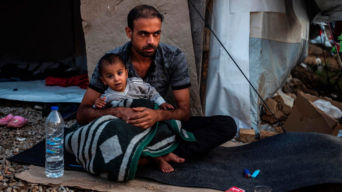Ein Mann sitzt mit einem Kind vor einer Unterkunft in Moria: Mehr als 200 Migranten werden aufs griechische Festland gebracht.