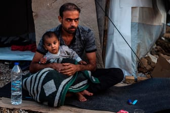 Ein Mann sitzt mit einem Kind vor einer Unterkunft in Moria: Mehr als 200 Migranten werden aufs griechische Festland gebracht.