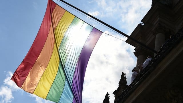 Eine Regenbogenfahne hängt an einem Gebäude.