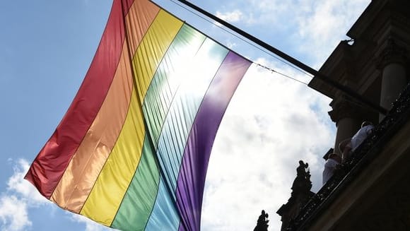 Eine Regenbogenfahne hängt an einem Gebäude.