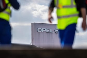 Zwei Männer in Sicherheitswesten gehen am Stammwerk von Opel vorbei: Der Autobauer Opel streicht in seinem Stammwerk Rüsselsheim für sechs Monate die Spätschicht.