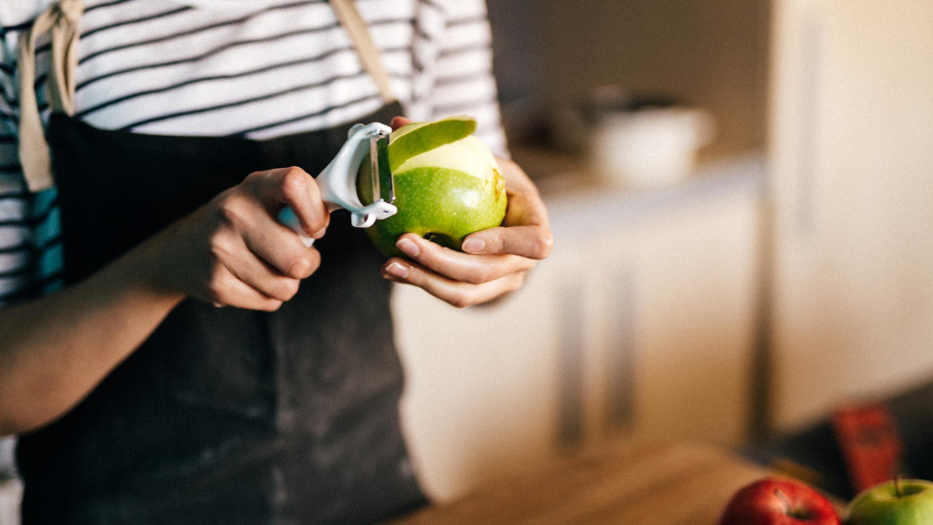 Eine Frau hält einen Apfel: So leicht lässt sich Obst mit dem Sparschäler schälen.