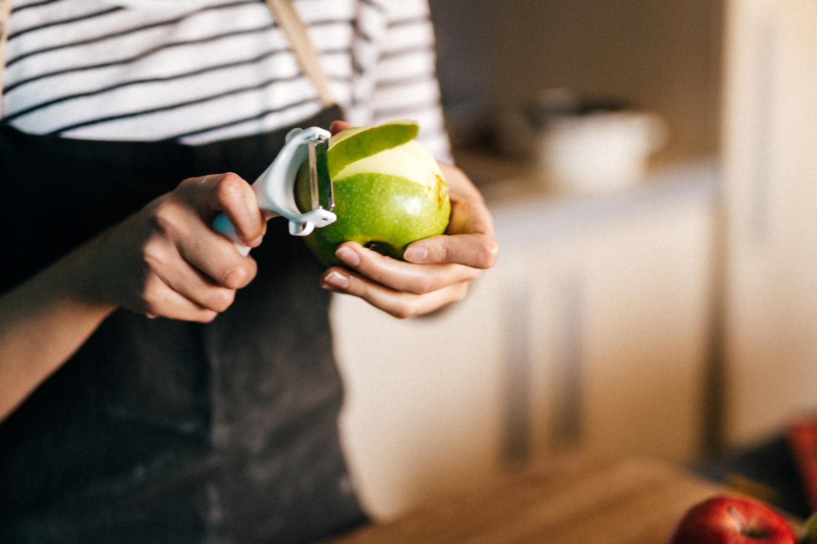 Eine Frau hält einen Apfel: So leicht lässt sich Obst mit dem Sparschäler schälen.