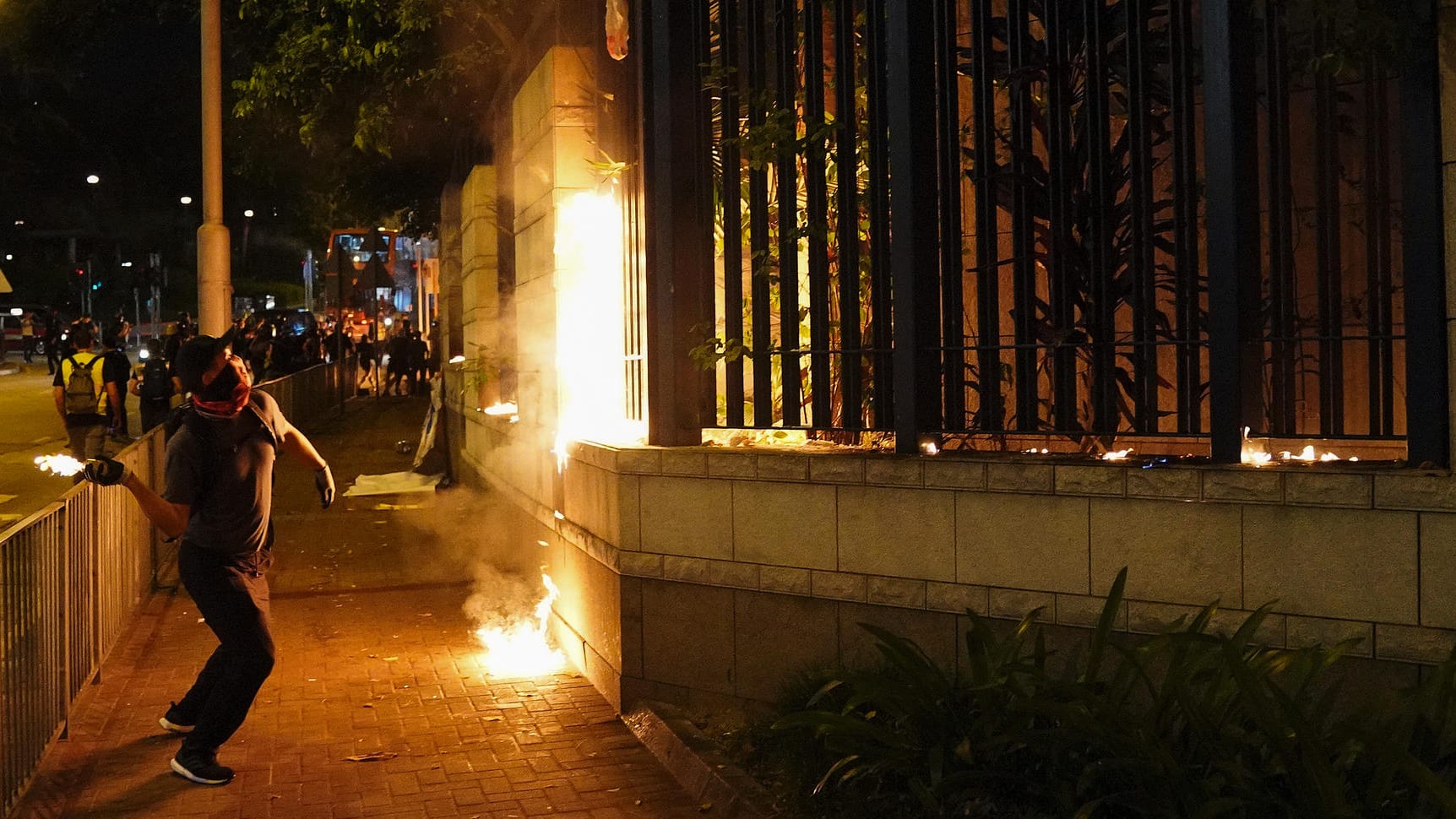 Ein vermummter Demonstrant in Hongkong wirft eine Brandbombe auf eine Polizeistation: Nach dem Schuss auf einen Demonstranten gehen die Proteste weiter.