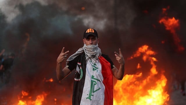 Ein Demonstrant zeigt vor lodernden Flammen das Siegeszeichen. Ein Demonstrant zeigt vor lodernden Flammen das Siegeszeichen.