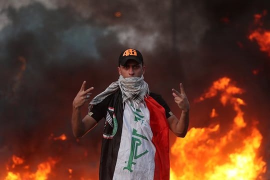 Ein Demonstrant zeigt vor lodernden Flammen das Siegeszeichen.