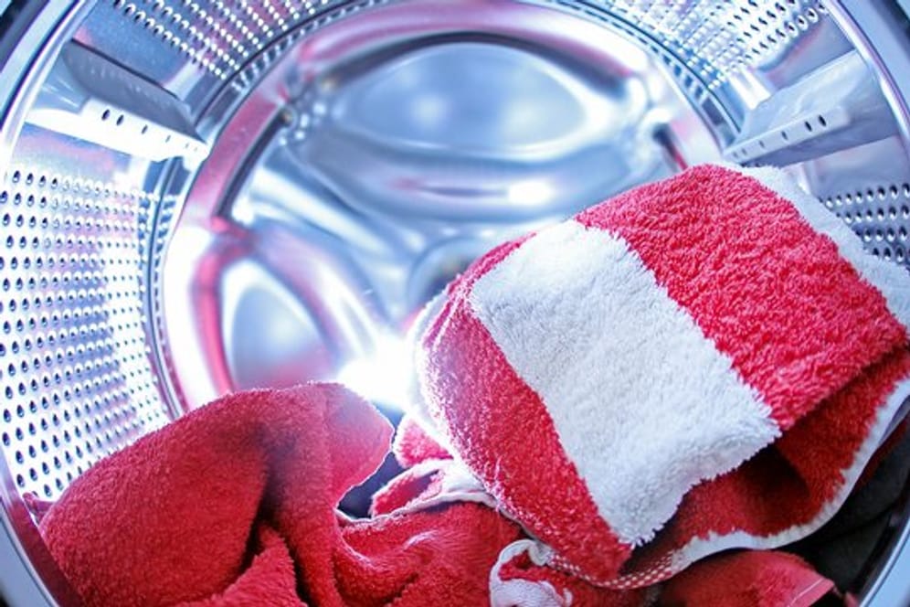 Wäsche liegt in einer Waschmaschine: Auch bei hohen Temperaturen können Erreger an Stellen wie Schublade, Pumpe oder Tür überleben.