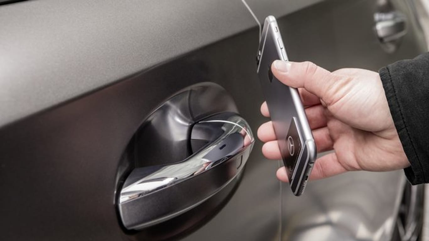 Ein Mann hält ein Smartphone an die Autotür: Mit der NFC-Technologie lässt sich wie hier bei Mercedes im digitalen Fahrzeugschlüssel-Sticker das Auto berührungslos öffnen, schließen und starten.