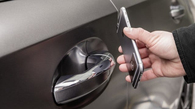 Ein Mann hält ein Smartphone an die Autotür: Mit der NFC-Technologie lässt sich wie hier bei Mercedes im digitalen Fahrzeugschlüssel-Sticker das Auto berührungslos öffnen, schließen und starten.