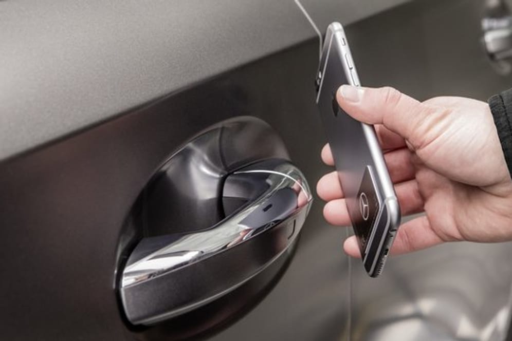 Ein Mann hält ein Smartphone an die Autotür: Mit der NFC-Technologie lässt sich wie hier bei Mercedes im digitalen Fahrzeugschlüssel-Sticker das Auto berührungslos öffnen, schließen und starten.