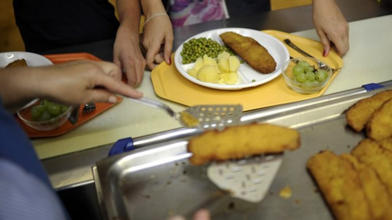 Eine Küchenhelferin legt an einer Gesamtschule ein Stück Fisch auf den Teller eines Schülers.