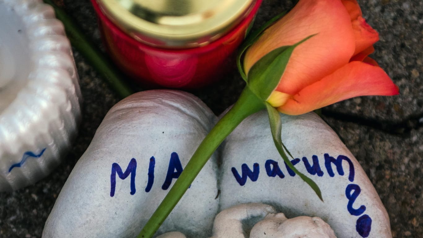 Kandel in Rheinland-Pfalz: Eine Skulptur in Form zweier Handflächen mit der Aufschrift "Mia warum?" und eine Rose liegen vor dem Drogeriemarkt, in dem ein 15-jähriges Mädchen im Dezember 2017 von ihrem Ex-Freund erstochen wurde.