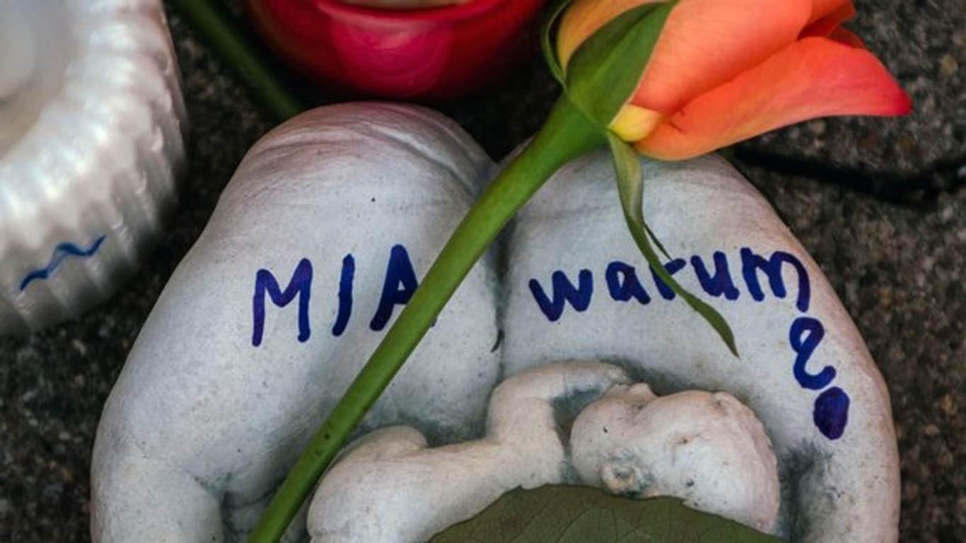 Eine Skulptur in Form zweier Handflächen mit der Aufschrift "Mia warum?" und eine Rose liegen vor dem Drogeriemarkt, in die 15-jährige Mädchen von ihrem Ex-Freund erstochen wurde.