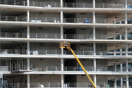 Arbeiter montieren von einer Hebebühne aus Teile an einem Neubau.