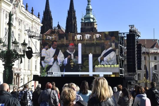 Fans stehen auf dem Hradschiner Platz und schauen auf einen Großbildschirm, auf dem die Trauerfeier für den Sänger Karel Gott im Prager Veitsdom übertragen wird.