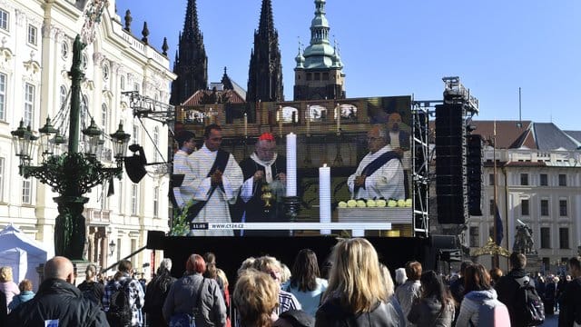 Fans stehen auf dem Hradschiner Platz: Sie schauen auf einen Großbildschirm, auf dem die Trauerfeier für den Sänger Karel Gott im Prager Veitsdom übertragen wird. F.