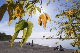 Goldener Oktober in Bayern: Ausflügler genießen am Ufer des Ammersees unter herbstlich gefärbten Bäumen den Sonnenschein.