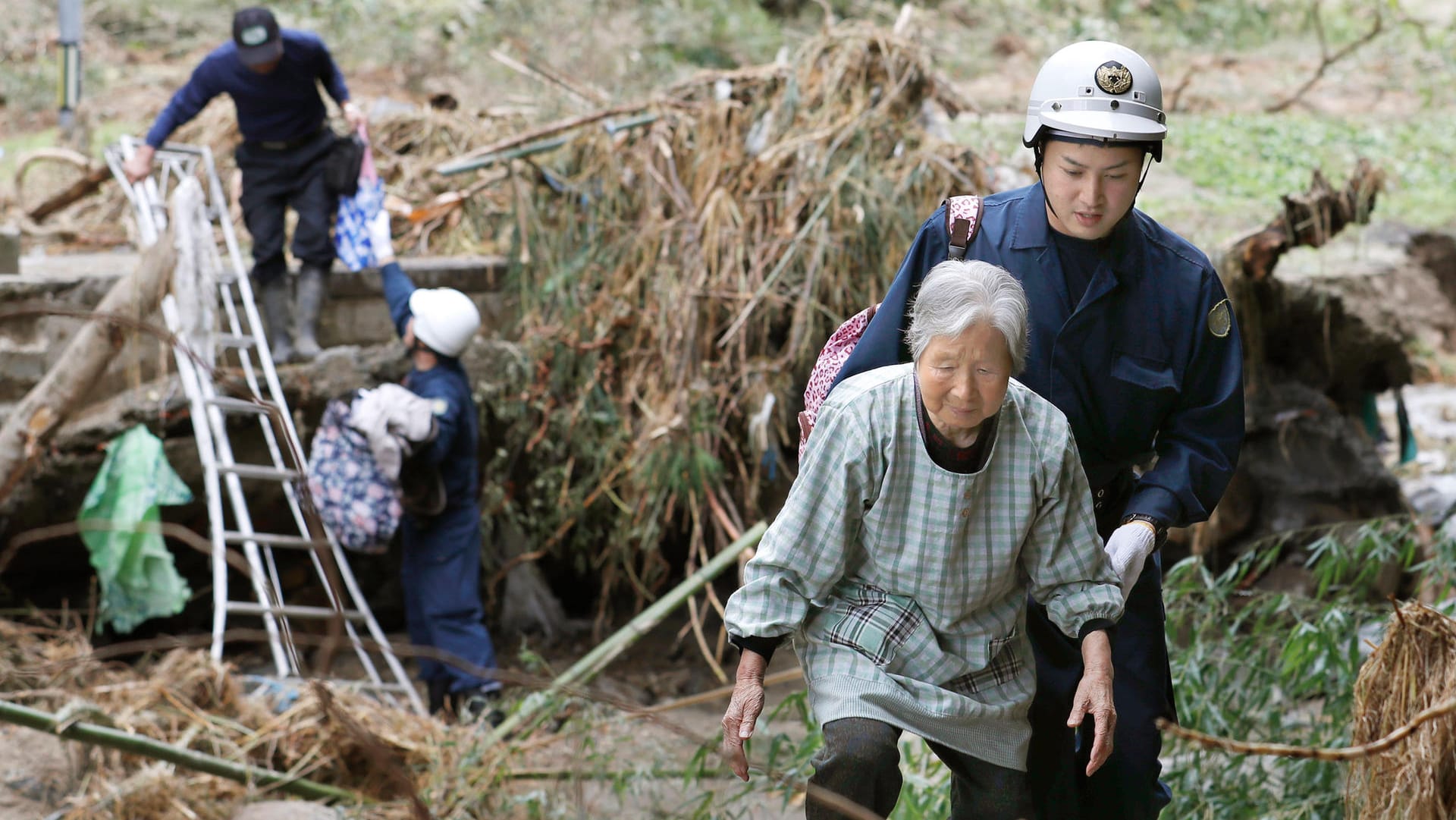 Rettungskräfte helfen Bewohnern über eine blockierte Straße: Die Zahl der Todesopfer nach dem verheerenden Taifun in Japan steigt weiter an. Rettungskräfte helfen Bewohnern über eine blockierte Straße: Die Zahl der Todesopfer nach dem verheerenden Taifun in Japan steigt weiter an.