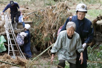 Rettungskräfte helfen Bewohnern über eine blockierte Straße: Die Zahl der Todesopfer nach dem verheerenden Taifun in Japan steigt weiter an.