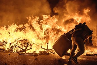 Barcelona am Dienstagabend: Ein Demonstrant wirft einen Mülleimer auf eine brennende Barrikade.