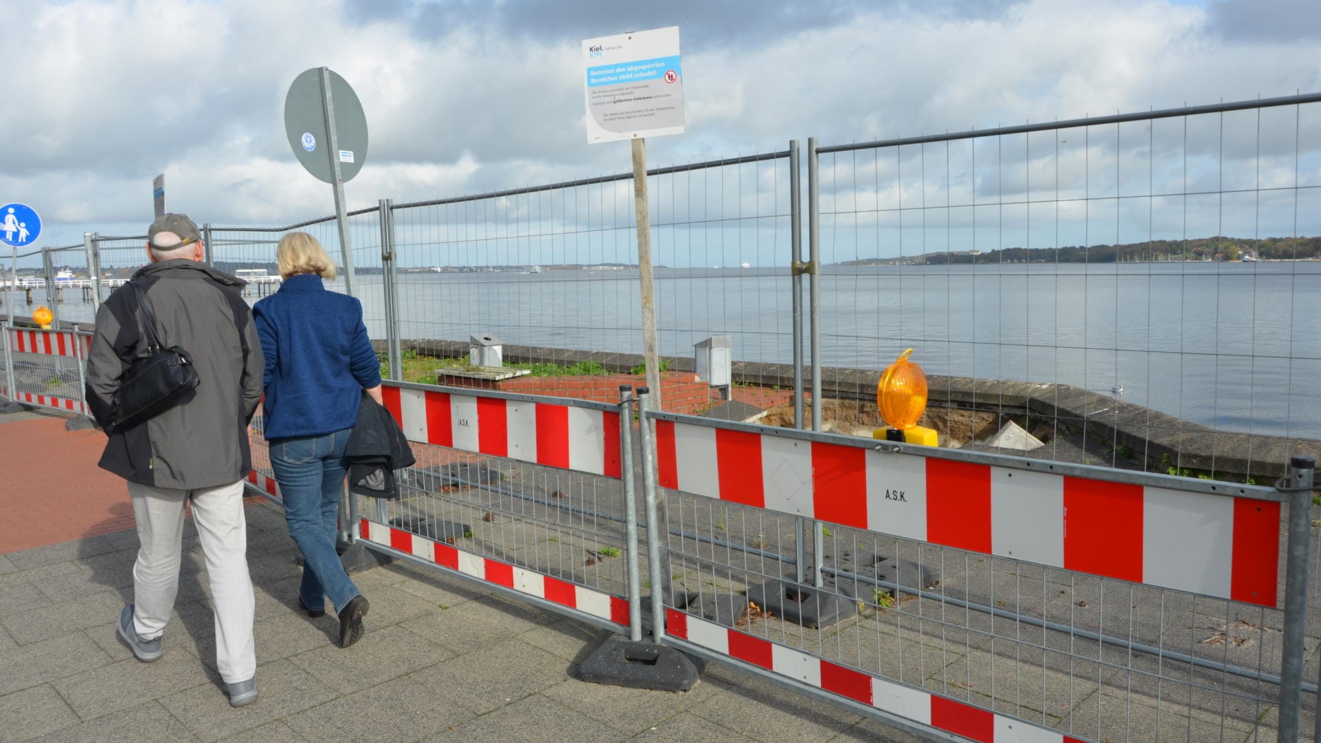 Zwei Passanten gehen am Bauzaun entlang: Seit drei Jahren verdirbt der Zaun den Blick aufs Wasser.