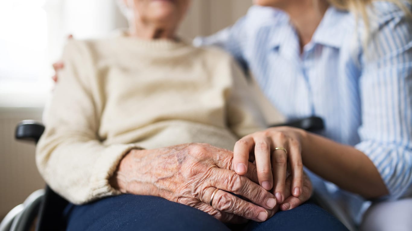 Pflegerin hält Hand einer älteren Dame: Einfühlsame Pflege ist wichtig, um das nötige Vertrauen aufzubauen.