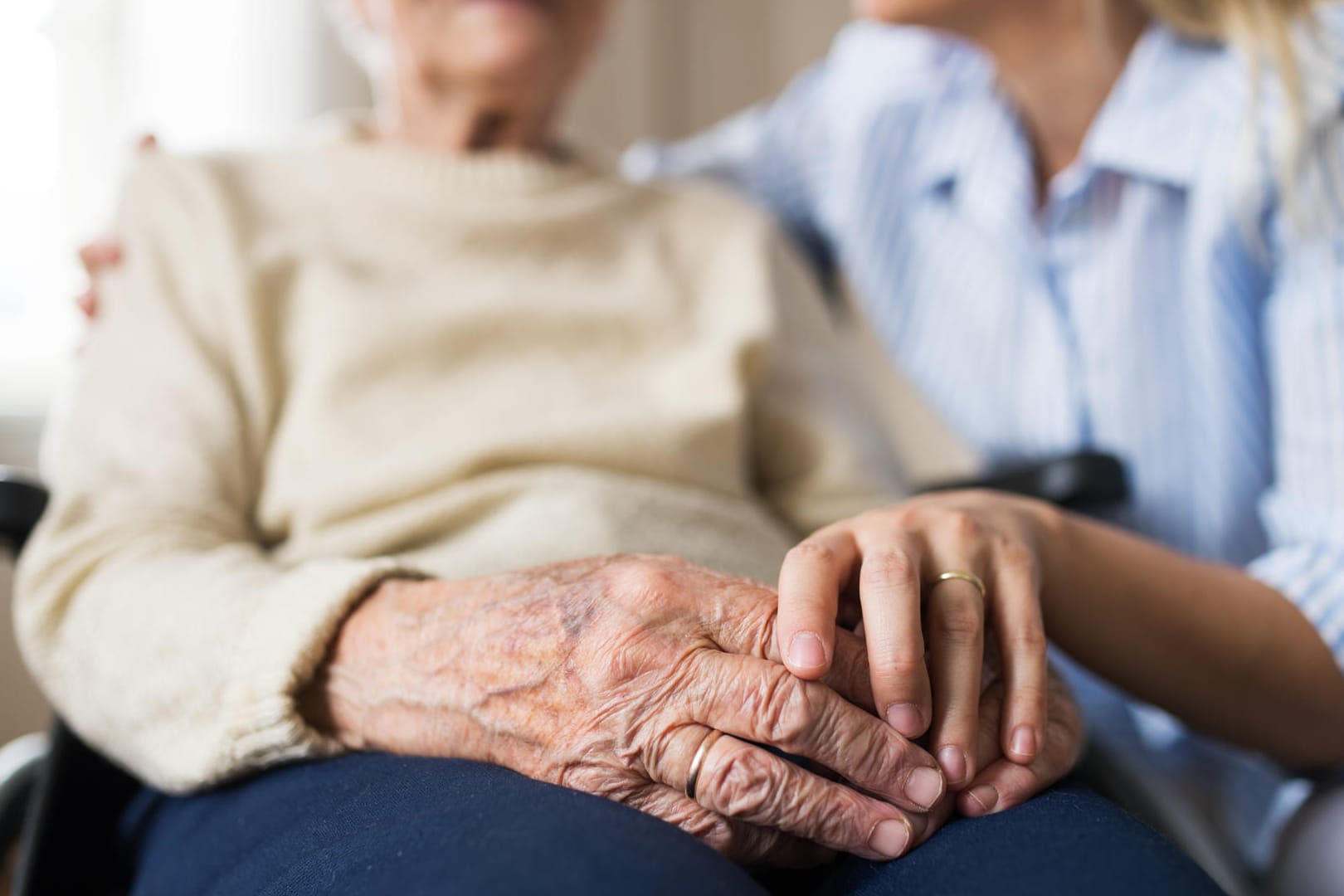 Pflegerin hält Hand einer älteren Dame: Einfühlsame Pflege ist wichtig, um das nötige Vertrauen aufzubauen.