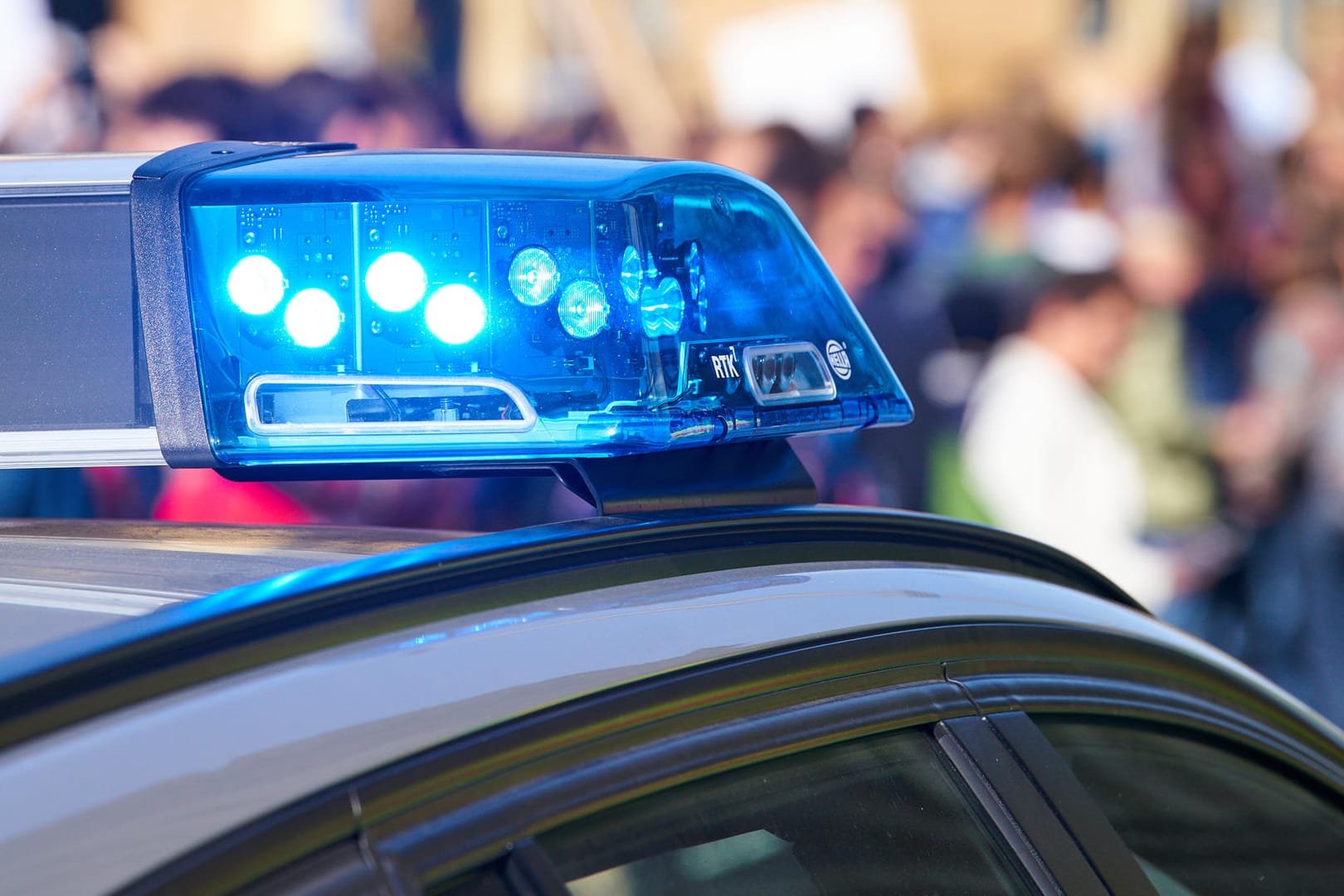 Ein Polizeiauto vor einer Menschenmenge (Symbolbild): Die Beamten in Magdeburg gaben das Einkaufszentrum nach drei Stunden wieder frei.