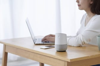 Eine Frau arbeitet an einem Tisch, auf dem ein Smart Speaker steht: Die vernetzten Lautsprecher lassen sich in Wanzen verwandeln.
