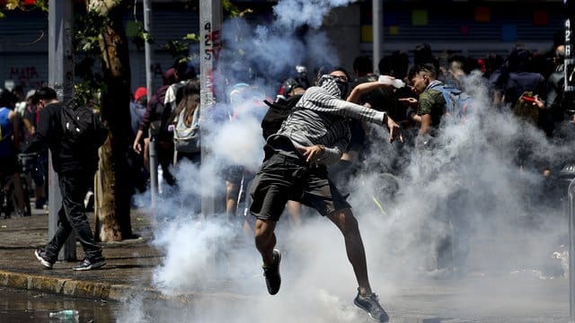 Ein Demonstrant wirft bei Protesten in Santiago de Chile eine Tränengasgranate zurück auf Polizisten. Ein Demonstrant wirft bei Protesten in Santiago de Chile eine Tränengasgranate zurück auf Polizisten.