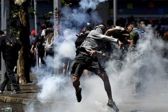 Ein Demonstrant wirft bei Protesten in Santiago de Chile eine Tränengasgranate zurück auf Polizisten.