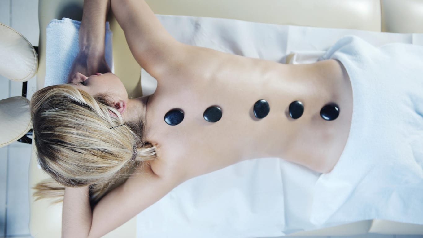 Frau mit schwarzen Steinen auf dem Rücken: Hot-Stone-Massagen bleiben beliebt. Heutzutage bietet der Wellness-Urlaub allerdings noch viel mehr Möglichkeiten.