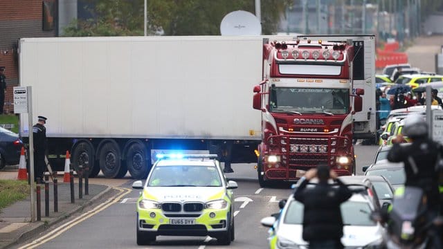 Ein Polizeiauto eskortiert den Lkw, in dem 39 Leichen gefunden worden waren, beim Verlassen des Waterglade Industrieparks. Ein Polizeiauto eskortiert den Lkw, in dem 39 Leichen gefunden worden waren, beim Verlassen des Waterglade Industrieparks.