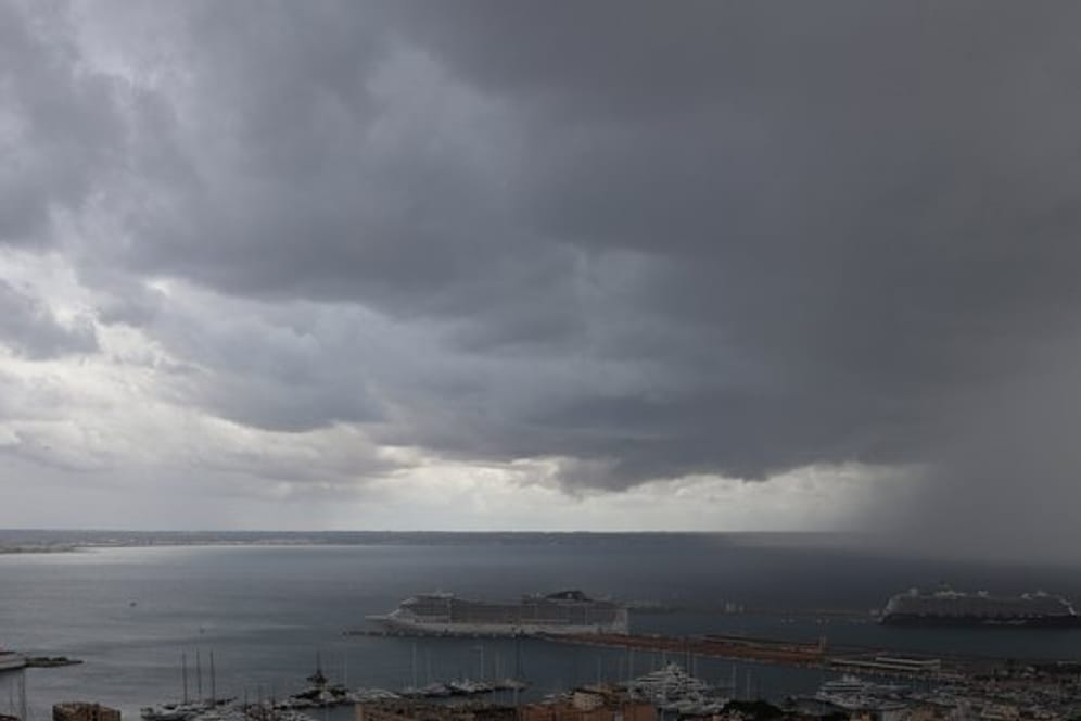 Dunkle Regenwolken hängen über der Bucht und dem Hafen, in dem zwei Kreuzfahrtschiffe liegen.