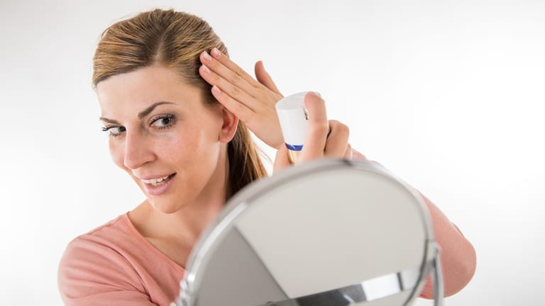 Eine Frau besprüht ihre Haare vor dem Spiegel: Stiftung Warentest hat die besten Trockenshampoos getestet.