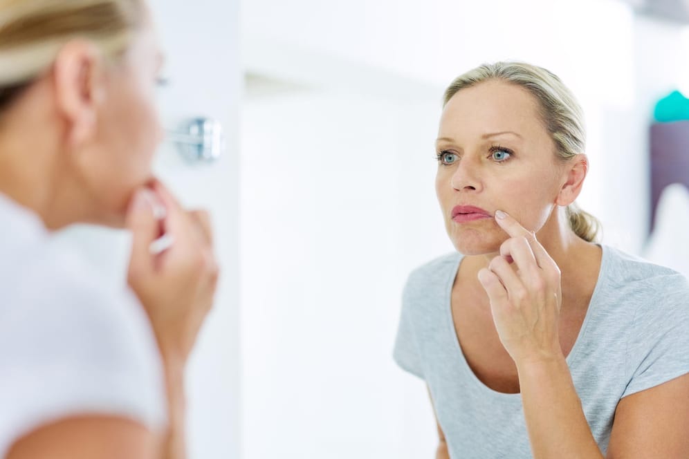 Eine Frau betrachtet sich im Spiegel: Tretinoin soll Falten glätten und die Hautstruktur verbessern.