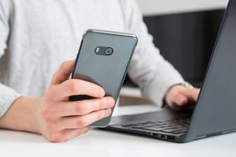 Ein Mann am Rechner mit Smartphone in der Hand: Ist das Internet ist zu langsam oder die Handyrechnung zu hoch, können Kunden ihre Rechte mit Hilfe von Musterbriefen einfordern.