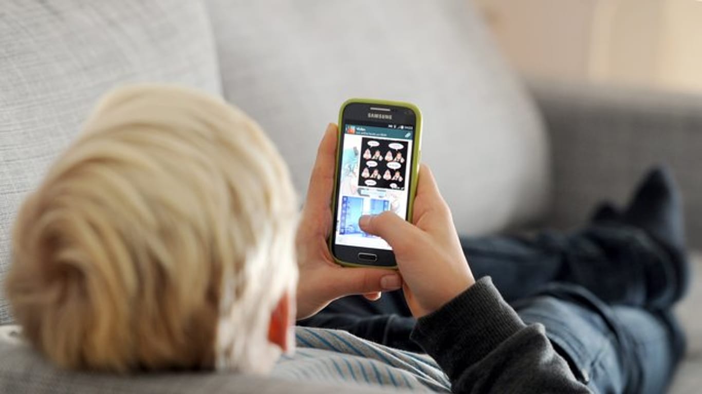 Ein Kind liegt auf einem Sofa und blickt auf sein Smartphone: Kinder sollten laut dem Chef des Berufsverbands der Kinder- und Jugendärzte zufolge nicht zu früh mit der Nutzung starten.