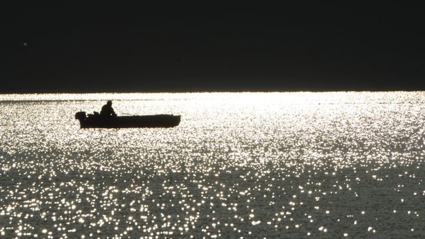 Ein Angler sitzt bei Sonnenaufgang in seinem Boot auf dem Bodensee bei Bodman.