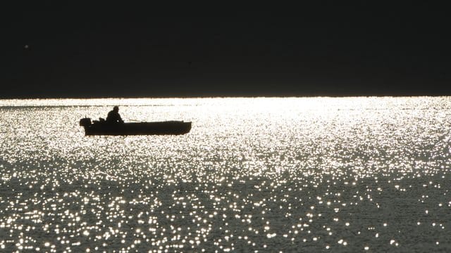 Ein Angler sitzt bei Sonnenaufgang in seinem Boot auf dem Bodensee bei Bodman.
