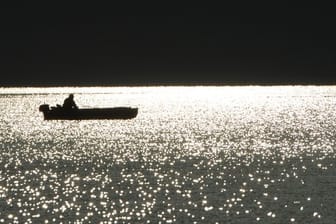 Ein Angler sitzt bei Sonnenaufgang in seinem Boot auf dem Bodensee bei Bodman.